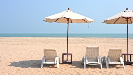 Tumbonas-De-Plástico-Blanco-Bajo-Sombrillas-En-Una-Playa-De-Arena-Tropical-En-Un-Día-Soleado