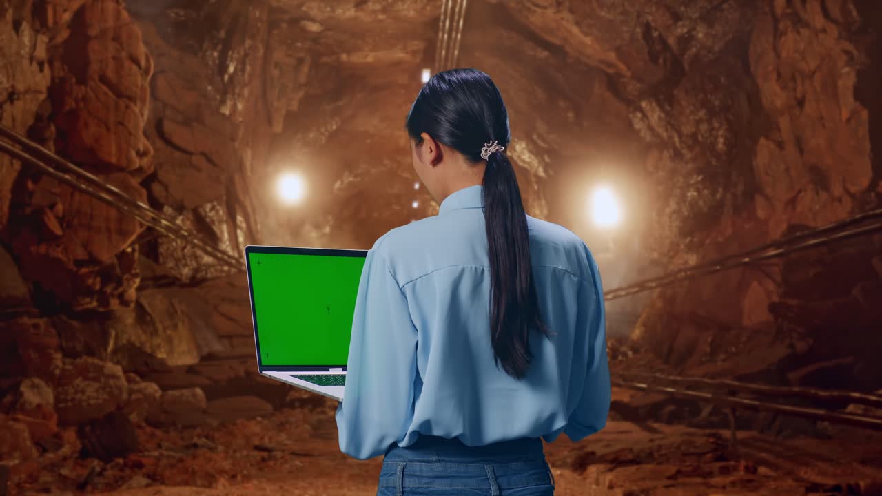 Back View Of Asian Female In Underground Mine Tunnel, Typing On Laptop'S Keyboard With Green Screen And Look At Mine Tunnel