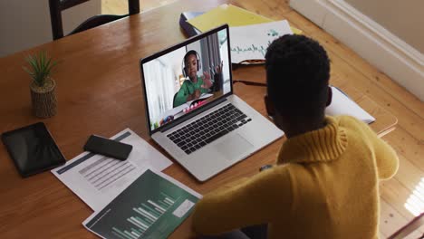 maestra afroamericana sentada en un escritorio usando una computadora portátil teniendo una lección escolar en línea
