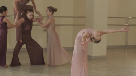 a group of young ballet students in black dancewear practicing positions in a spacious ballet studio with wooden flooring and wall-mounted barres. focused expressions and synchronized movements.