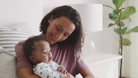 happy millennial african american mother sitting up in bed holding her baby, close up