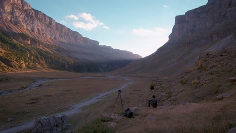 Back-view-of-young-Hiker-and-photographer-man-standing-next-to-a-tripod-and-sitting-down-autumn-in-Ordesa-National-Park,-Spain