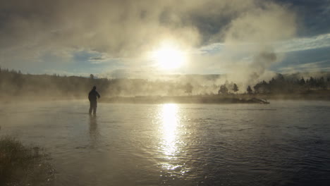 side angle silhouette of a man with fishing rod in his hand standing in river illuminated by shiny sunlight and smoke, pov