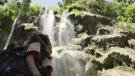 young caucasian woman with adventuring backpack stares up at tropical tumalog waterfall in phillippines