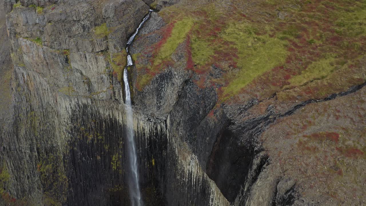 inclinación aérea hacia abajo que muestra una impresionante cascada que se derrumba en un barranco islandés durante un día nublado - paisaje volcánico de musgo