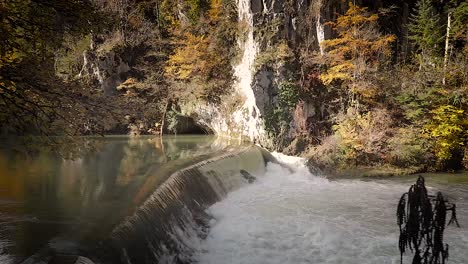 Aerial shot of waterfall near Arête des Sommêtres crest near Le Noirmont, canton Jura, Switzerland. Stream running fast in summer green forest. Small waterfall. Stones and logs covered with moss.