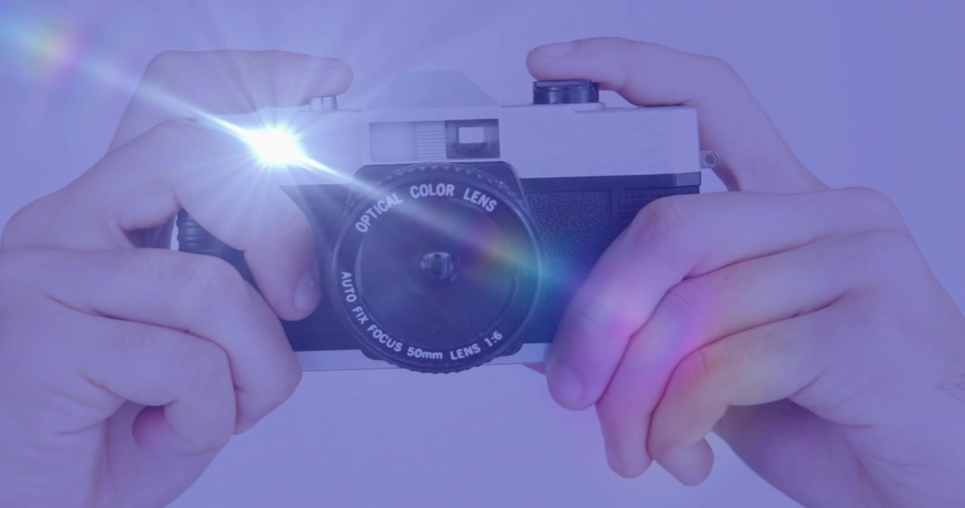Mani che centrano una fotocamera da 35mm su uno sfondo viola, con il flash integrato che si attiva e crea bagliori.
