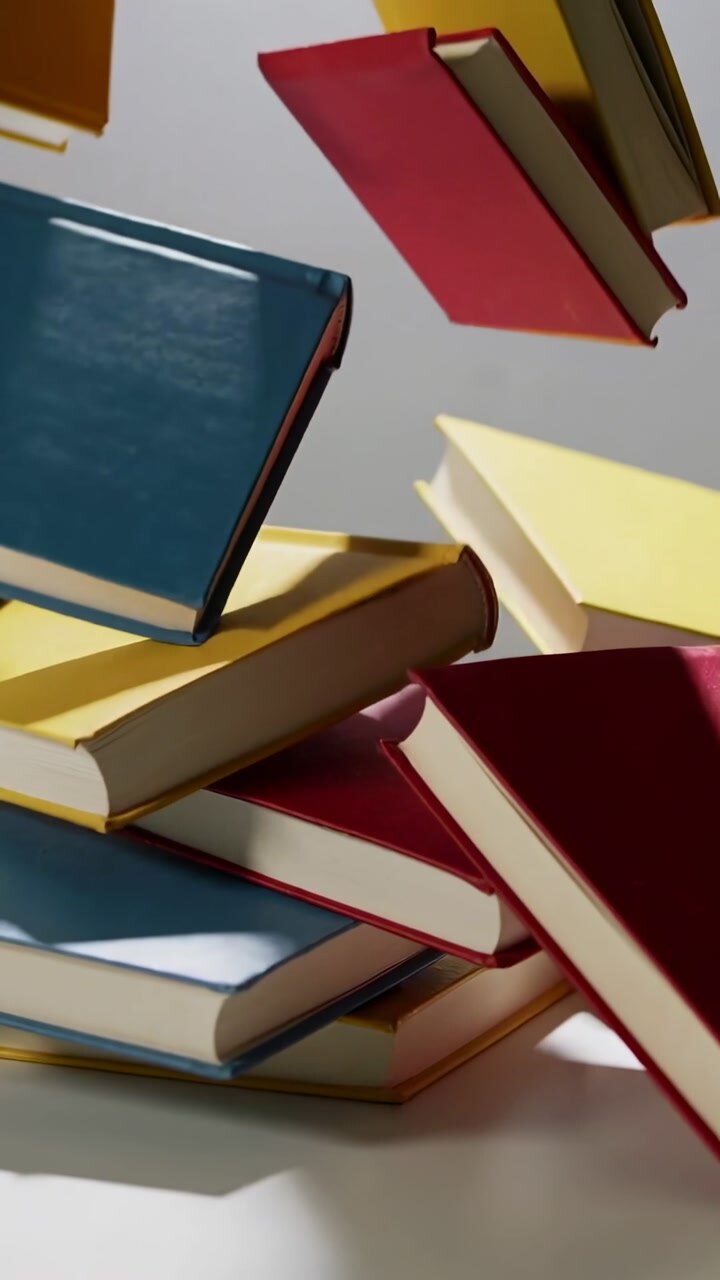 Vertical video: Collapsing hardcover books tumbling on tabletop, triggered by falling blue book