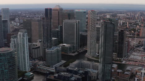 Aerial-slide-and-pan-footage-of-modern-business-urban-district-Canary-Wharf-with-group-of-tall-skyscrapers-in-evening.-London,-UK