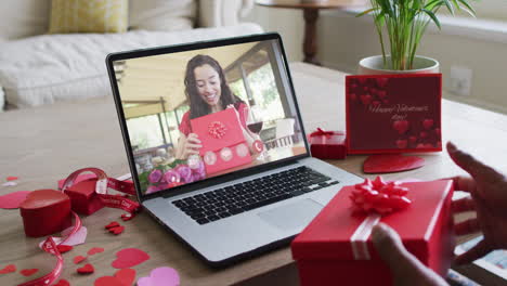 happy biracial woman with vitiligo opening gift and making valentine's day video call on laptop