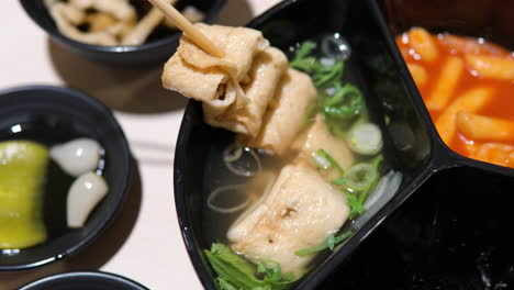 traditional korean restaurant set with odeng, tteokbokki, rice covered in seaweed kim, side dishes - mushrooms udon, yellow pickled radish danmuji, and rakkyo - top revealing from close-up