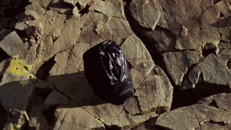 black trash bag lay on a rocky beach