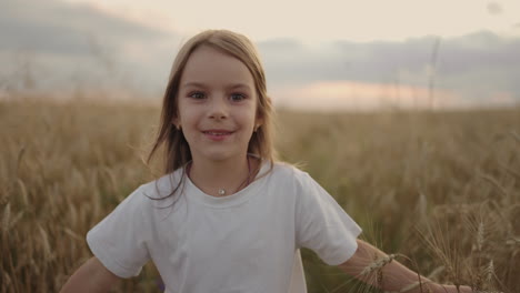 Slow-motion-a-little-girl-of-4-5-years-old-runs-in-a-field-at-sunset-looking-at-the-camera-happy-and-free.-Happy-childhood.-Girl-Running-In-Field-At-Sunset