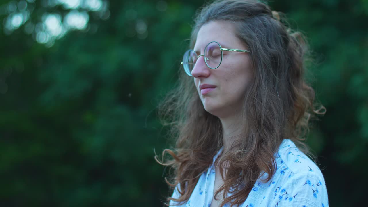 A young woman outdoors, with glasses and eyes closed while some mosquitoes flying around