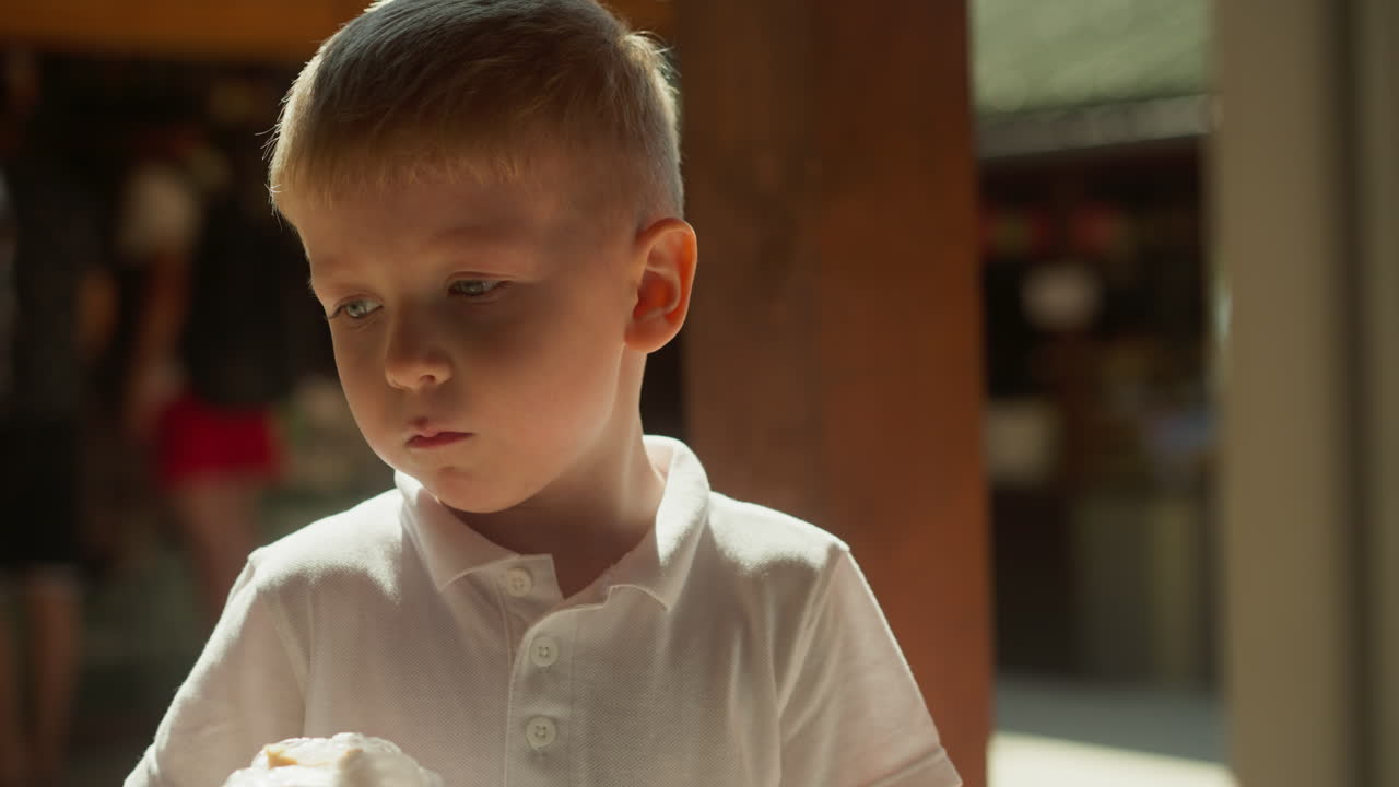 만족한 유아 소년은 따뜻한 날씨에 흐릿한 배경의 건물 지붕 아래 서서 점심을 먹습니다. 점심 시간에 음식을 먹습니다. 배고을 만족시키고 평온한 분위기