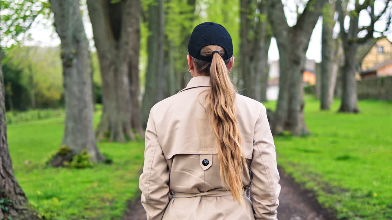 Happy woman in beige trench coat walking in spring park. Pretty blonde smiling woman enjoying life and breathing fresh air