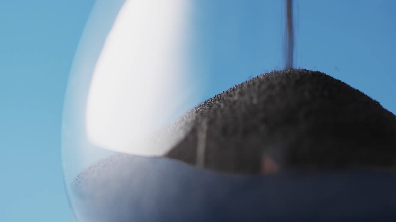 파란색 배경에 복사 공간과 함께 흘러내리는 검은 모래와 함께 모래시계의 클로즈업 비디오