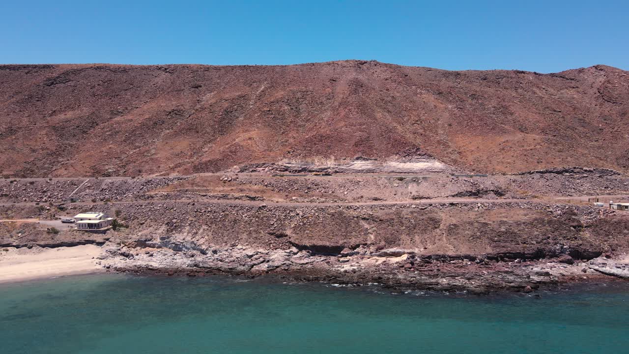 retiro aéreo de la pendiente erosionada rocosa hacia la playa con agua azul verde brillante