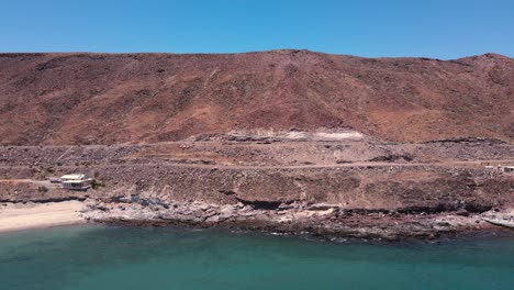 Luftaufnahme-Von-Felsigen-Erodierten-Abhang-Hinunter-Zum-Strand-Mit-Glitzerndem-Grün-blauem-Wasser