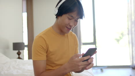 십대 아시아 소년은 집에서 드폰으로 음악을 즐긴다.