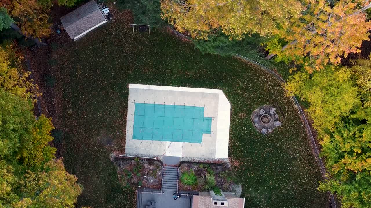 Fall trees with changing leaves and beautiful Autumn colors shown over a gorgeous suburban yard complete with winterized pool
