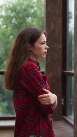 woman gazes out of window on terrace. woman in checkered shirt expression reflects of weight of thoughts during difficult period of life. inner turmoil palpable