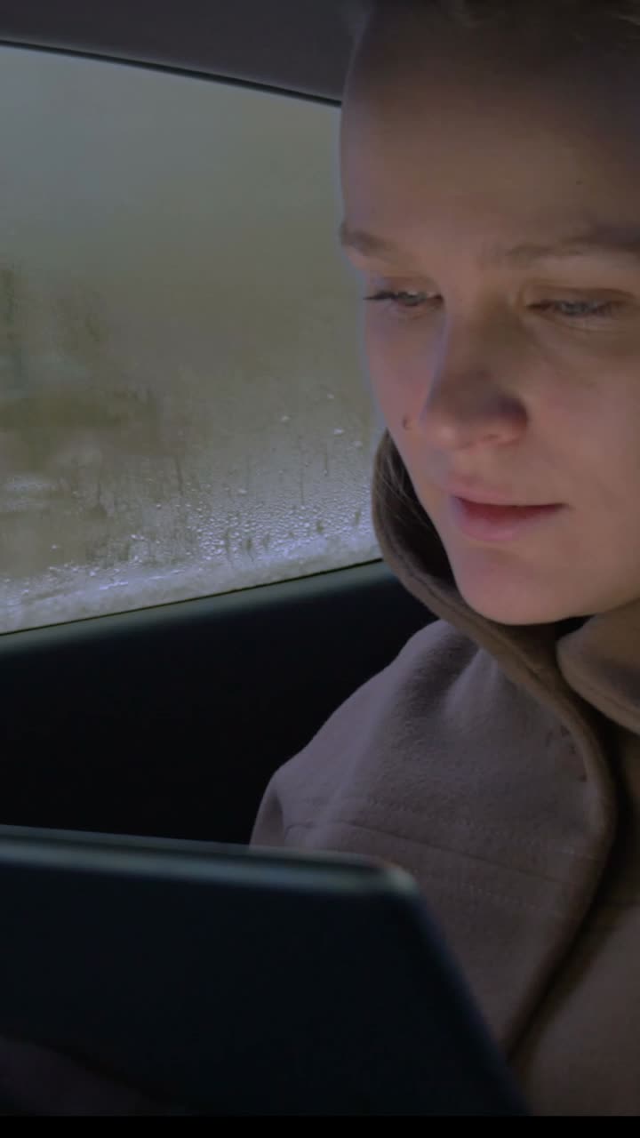 Woman using a tablet in a car on a rainy day