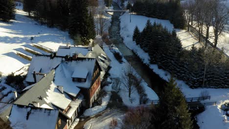 Aerial-drone-backward-moving-shot-over-beautiful-snow-covered-cottages-along-the-Bielice-mountain-slope,-Poland-during-cold-snow-covered-winter-day