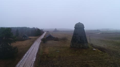 Foggy rural road leads to abandoned windmill ruins in a Latvian village Ķāķišķe