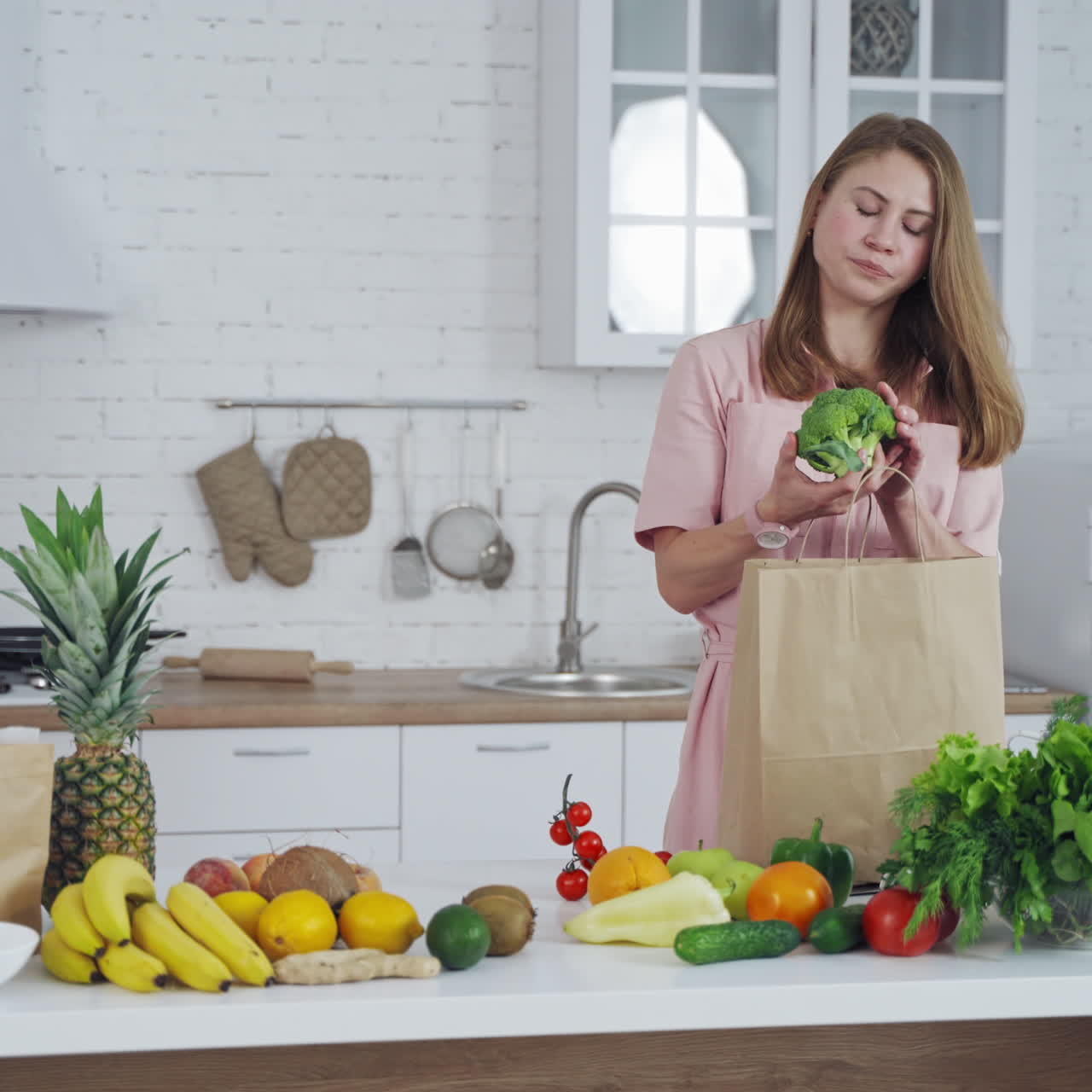 Young woman unpacking shopping bag, taking out green broccoli. Kitchen background and pretty girl putting fresh vegetables on the table. Healthy food.