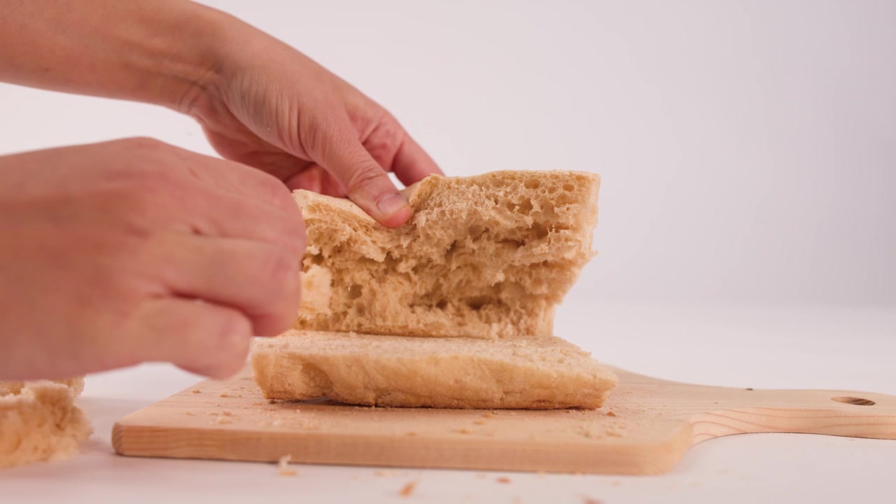 Close-up shot of hands separating crusty sourdough bread on a wooden board against white.