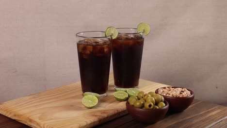 chilean piscola drink typical summer cocktail of chile glass with ice wooden board and lemons in bright background with selective focus