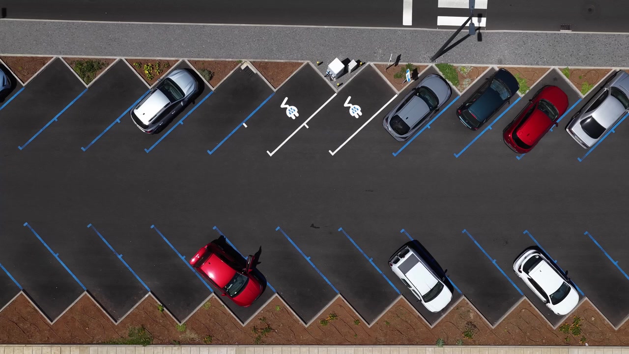Une vidéo nette par drone montre des symboles de bornes de recharge pour véhicules électriques sur un parking public propre à Madère, Portugal, avec des voitures colorées et un agencement géométrique
