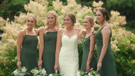 bride and bridesmaids posing with arms around each other in garden slow motion