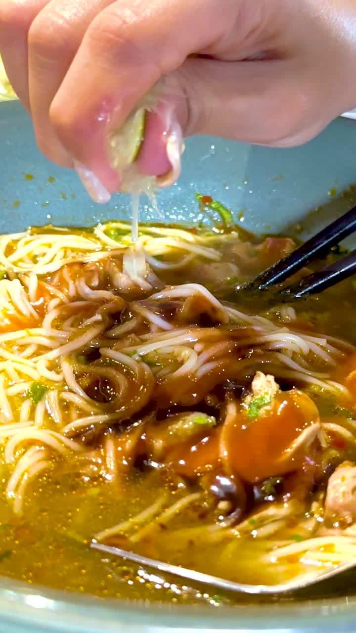 Una mano spreme del lime su una ciotola di pho vietnamita, esaltandone i sapori. L'illuminazione intensa mette in risalto gli ingredienti vivaci e la presentazione fresca.