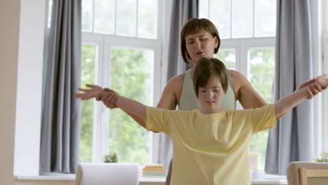 mujer sosteniendo las manos de su hija con síndrome de down por enseñarle una postura de yoga