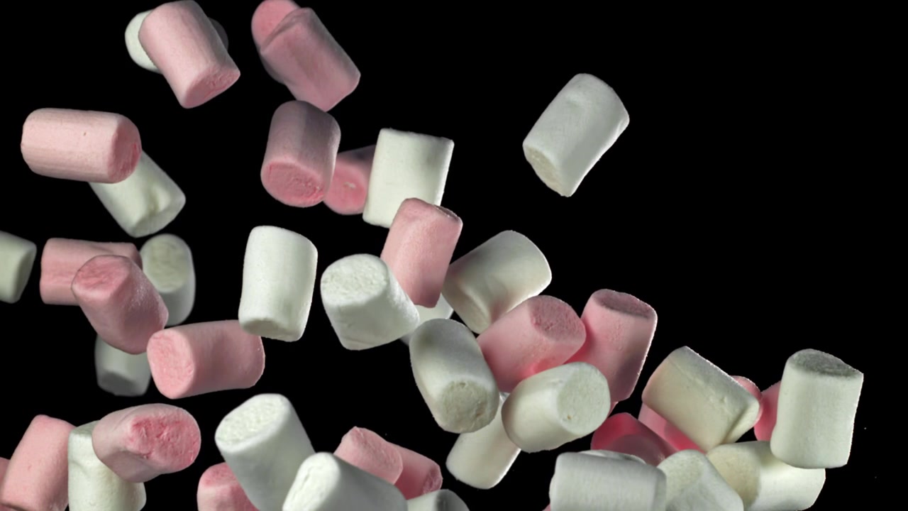 Marshmallow rosa e bianchi che cadono al rallentatore su sfondo nero.