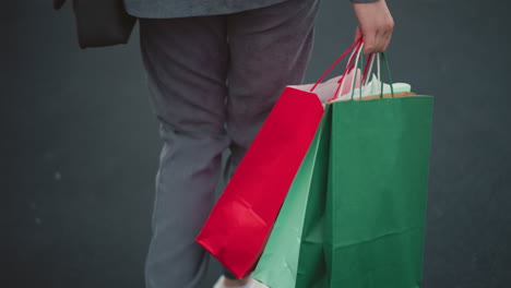 close-up back view of a woman in casual grey attire walking down stairs while carrying colorful shopping bags, carefully stepping on a black carpet stairs