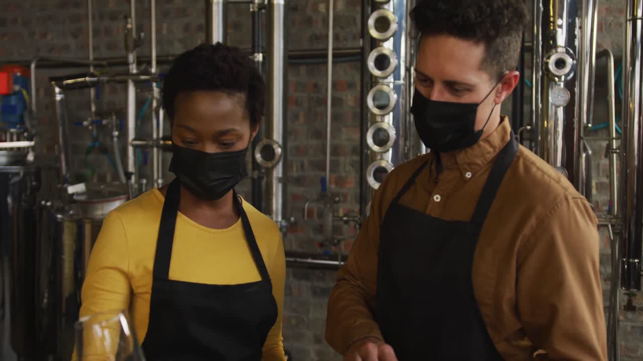 diversos colegas masculinos y femeninos con máscaras faciales en la destilería de ginebra, comprobando el producto y usando la tableta