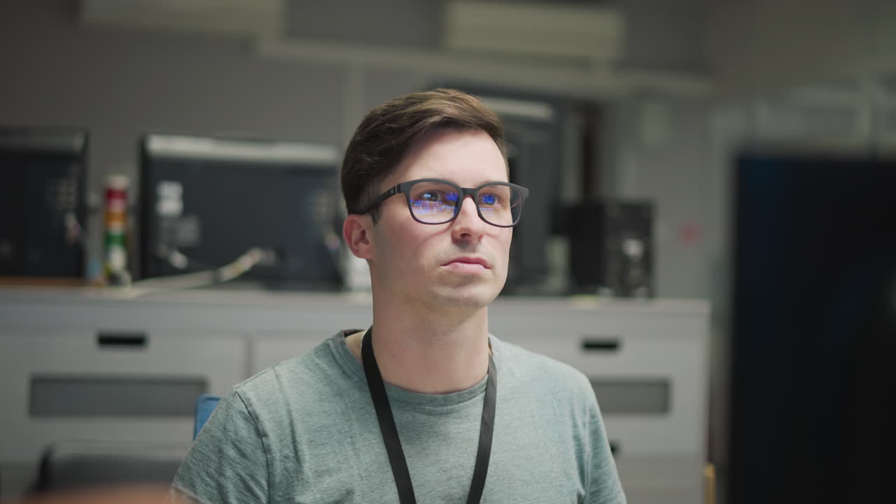 Person working at computer, focused on multiple monitors in modern office environment, wearing glasses, managing system or network tasks, tech workspace, computer setup with multiple screens