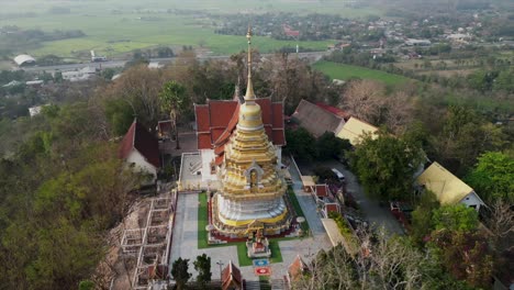 aerial view of a golden pagoda and traditional thai temple complex nestled on a lush, forested hilltop