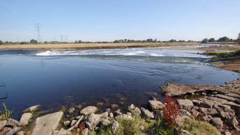 water going over the river trent weir with rocky forground, by ratcliffe on soar power station. wide shot