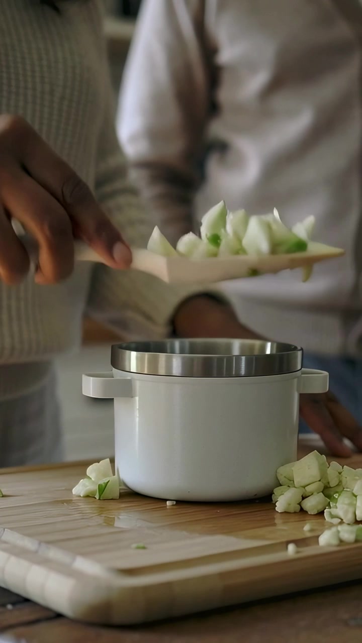 Vertical video: Chopping as knife hitting board woman in cream knit sliding cubes into cup for meal