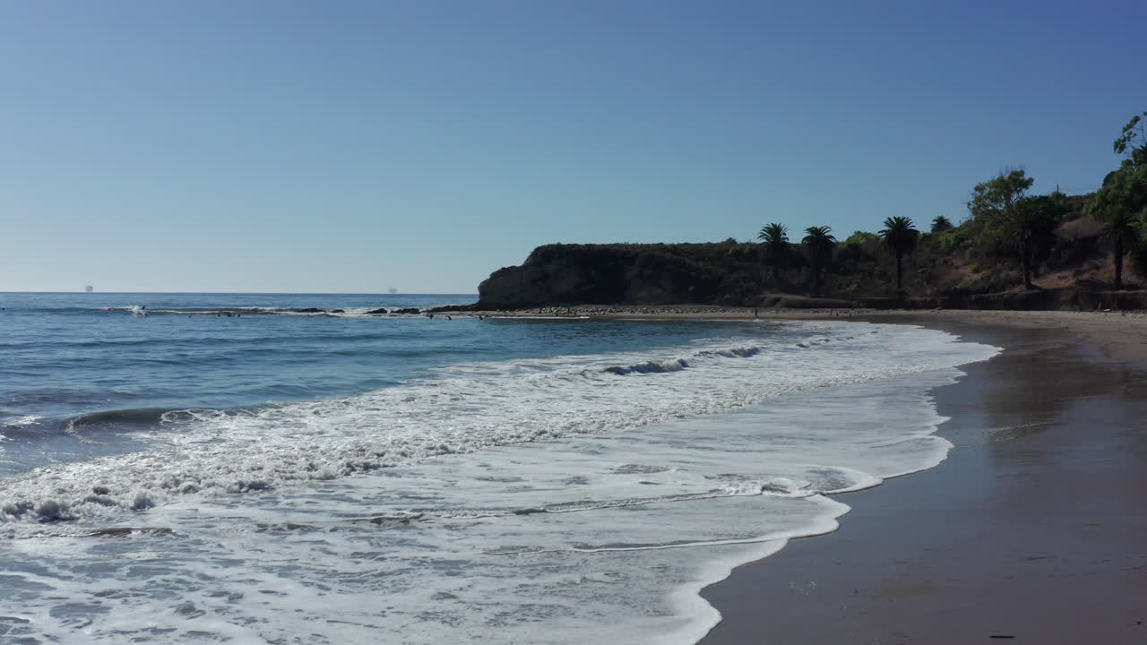 Carrellata su un'idilliaca spiaggia californiana con onde dolci e scogliere