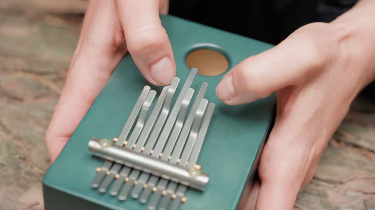 Extreme close up of white person hands in dark outfit plucking metal tines on small green thumb piano, focusing on movement, rhythm, and tactile texture, expressing calm creativity