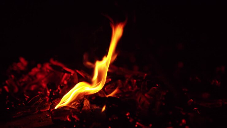 Charcoals with little flame burning on. the embers are moved and tiny sparks fly up. Close up. Black backdrop.