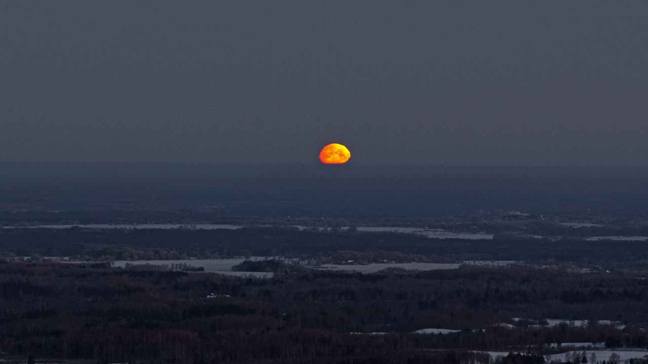 Grande lua vermelha nascendo sobre paisagem de inverno nevada sob céu noturno escuro, afastamento aéreo.