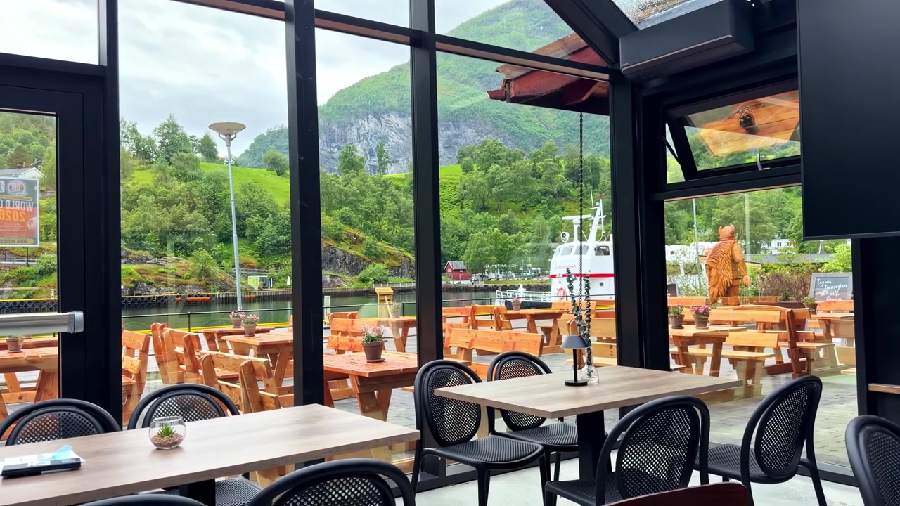 Modern cafe interior with glass walls overlooking outdoor seating and fjord scenery