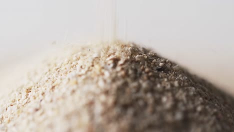 Video-of-close-up-of-sand-grains-pouring-into-heap-and-copy-space-on-white-background