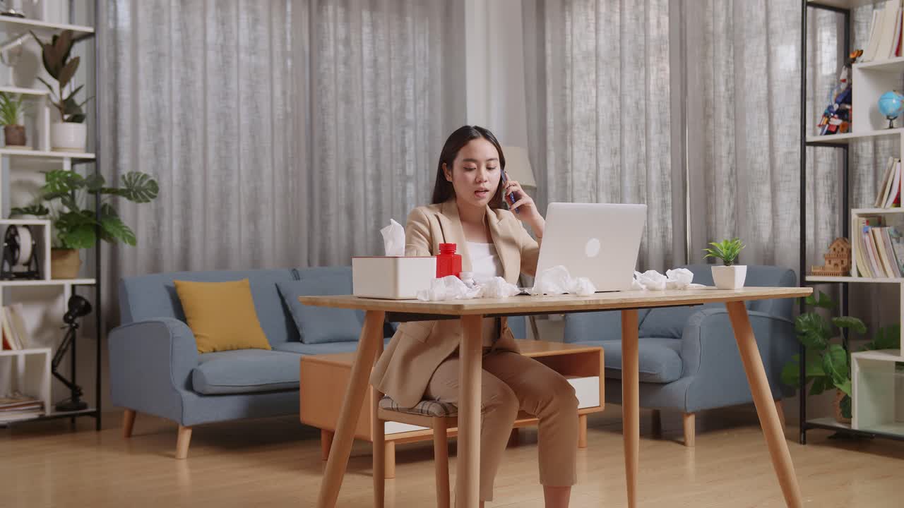 아시아 여성 사업가 가 집 의 거실 에서 노트북 을 사용 하면서 온도계 를 들고 전화 를 하고 있다